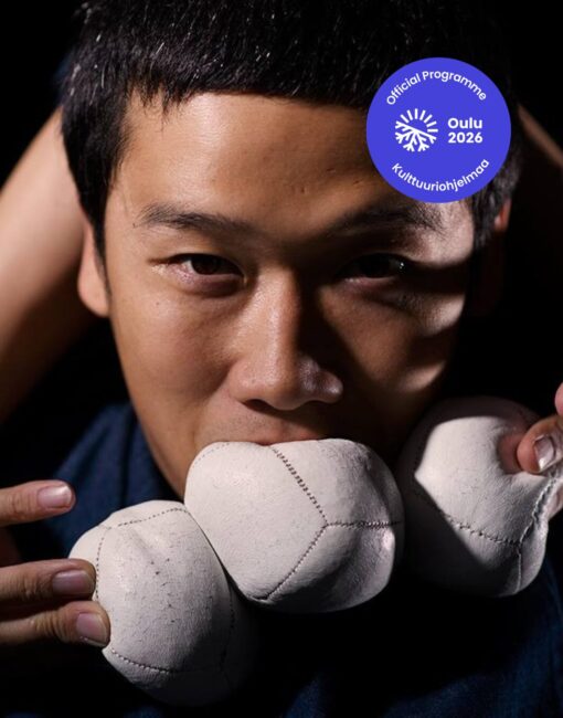 Japanilainen miesoletettu katsoo kameraan lähikuvassa. Hänellä on pallo suussa ja molemmissa käsissä.