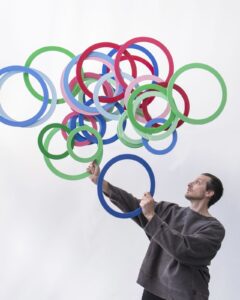 Jonglööri Jay Gilligan heittää valtavan määrän värikkäitä renkaita ilmaan.