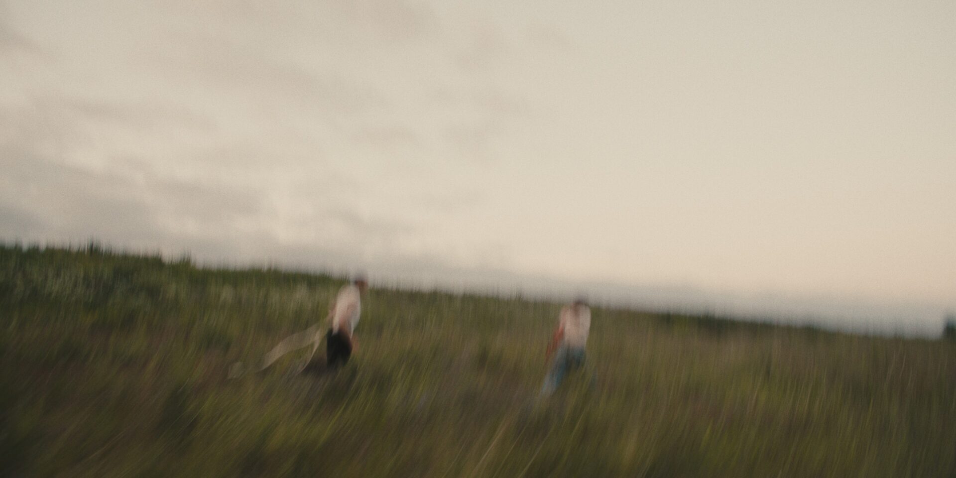 Nainen ja mies juoksevat sumuisella niityllä. Kuva on epätarkka, niin kuin kamera olisi heilahtanut.