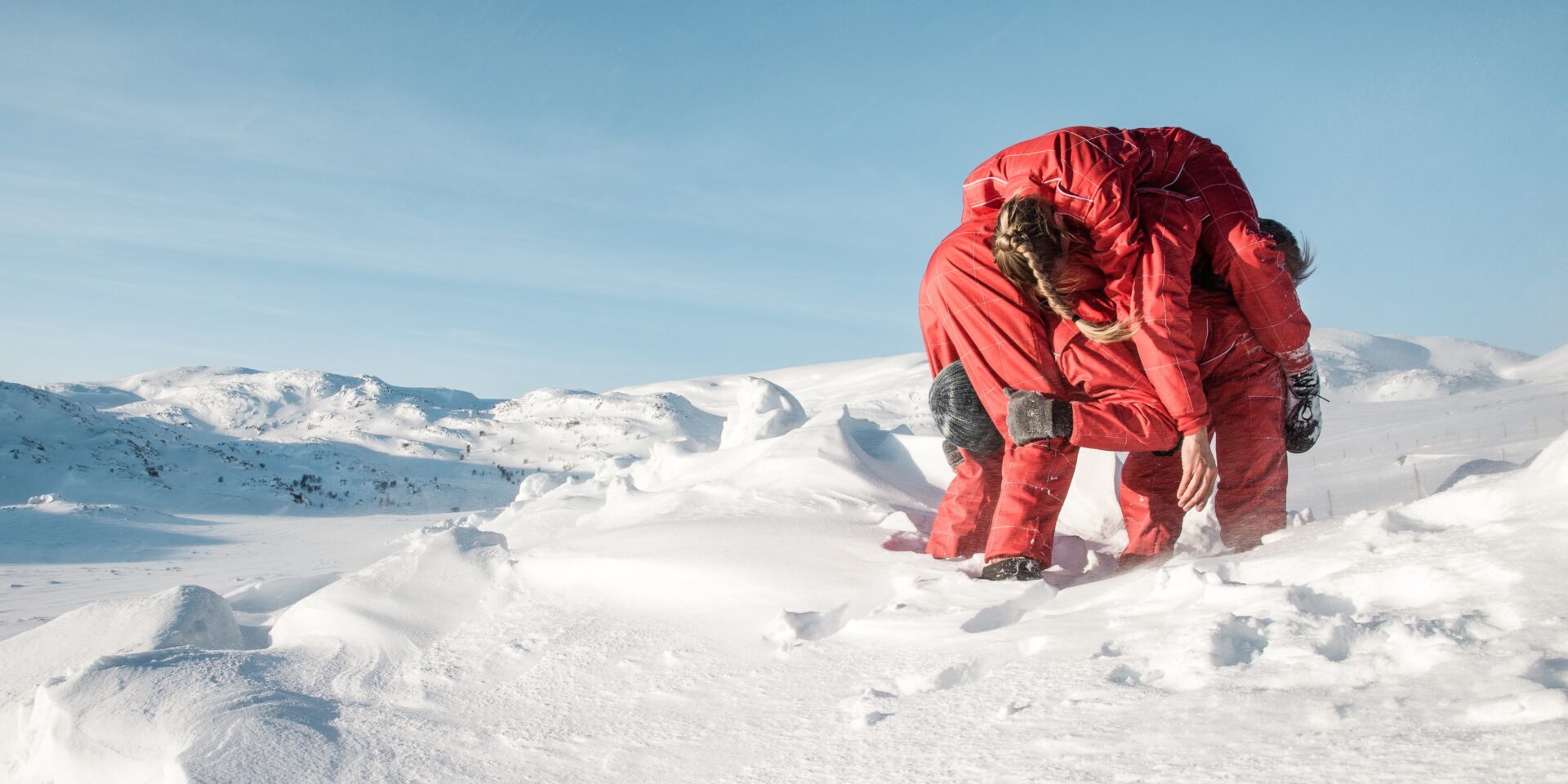 Kolme sirkustaiteilijaa retkottaa kasassa lumihangessa punaisissa toppavaatteissaan.