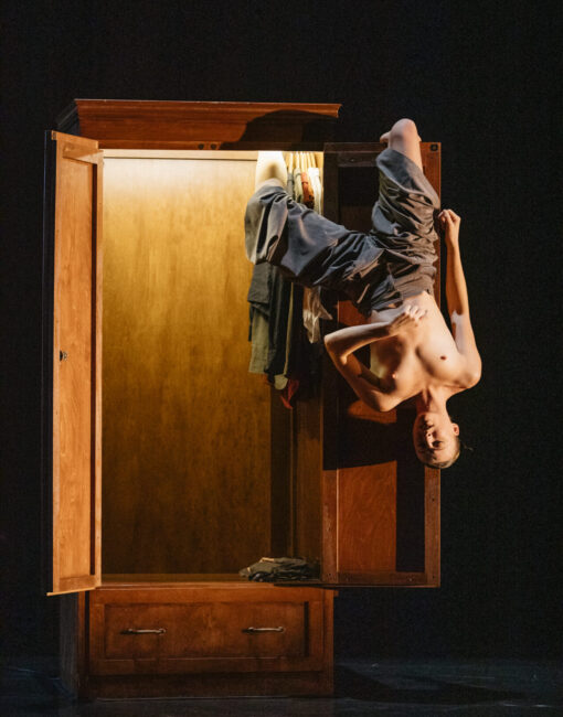 Ihminen roikkuu pääalaspäin kaapin ovesta ilman paitaa.