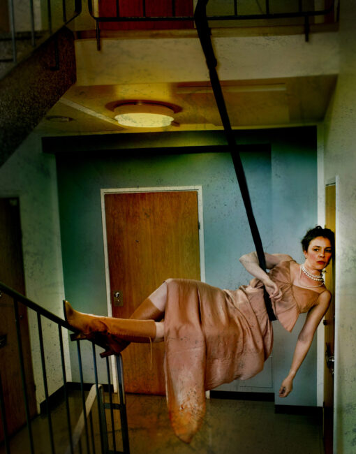 Nainen roikkuu rappukäytävässä ylemmän kerroksen kaiteeseen kiinnitetystä narusta.